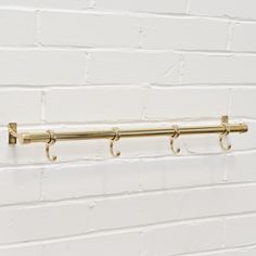 a white brick wall with three brass hooks on the side and one is holding two coats of coat hangers