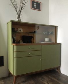 a green cabinet sitting on top of a hard wood floor next to a vase filled with flowers