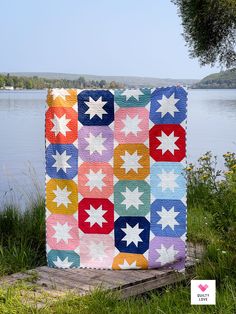 a colorful quilt sitting on top of a wooden platform next to a body of water