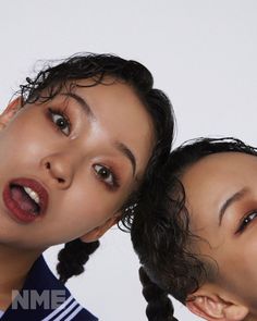 two young women with braids are looking at the camera while one is brushing her hair