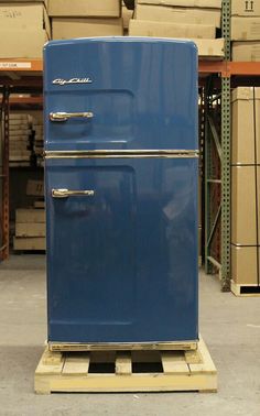 an old blue refrigerator sitting on top of a pallet in a warehouse with boxes behind it