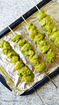 several skewers of green food on tin foil lined up in the shape of squares