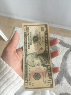 a person holding up a one dollar bill in their hand on a carpeted floor