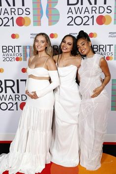 three women in white dresses standing on a red carpet at the brity awards 2021