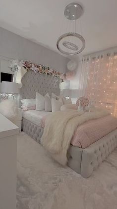 a bedroom decorated in white and pink with lights on the windowsills, a bed covered in fluffy blankets and pillows