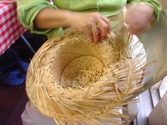 a woman sitting at a table making a straw hat