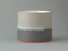 a white and grey vase with red trim on the bottom is sitting in front of a gray background