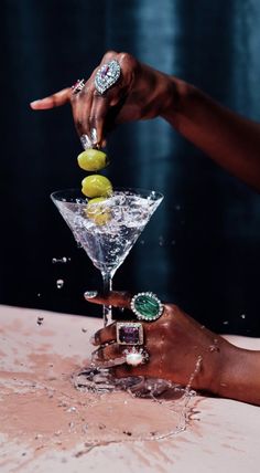 two hands are reaching into a martini glass filled with limes and lemonade slices