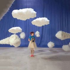 a woman standing in front of a blue backdrop with white clouds floating over her head