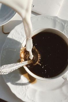 a cup of coffee is being poured into the saucer with a spoon on it