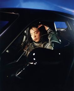 a woman sitting in the driver's seat of a car with her hand on her head