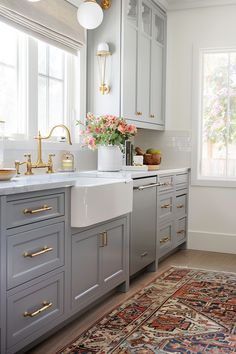 a kitchen with gray cabinets and gold hardware on the handles, sink, and rug