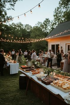 a long table filled with food on top of a lush green field next to a white house