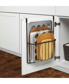 an open kitchen cabinet with dishes and utensils in the bottom drawer, next to a trash can