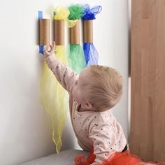 a baby playing with some toilet paper rolls on the wall next to it's head