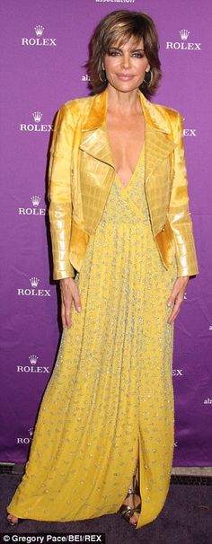 a woman in a yellow dress and gold jacket posing for the camera at an event