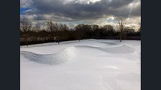 a snow covered field with trees and clouds in the background