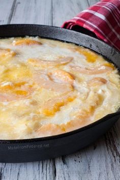 an omelet is sitting in a black pan on a white wooden table next to a red checkered napkin