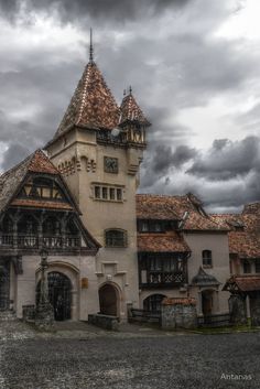 an old building with two towers and a clock on the top is surrounded by dark clouds