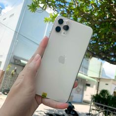 a person holding up an iphone in front of a building with trees on the street