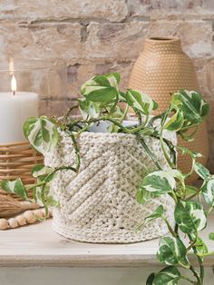 a white basket sitting on top of a wooden table next to a candle and potted plant