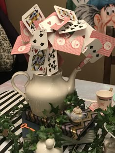 a table topped with cards and a teapot on top of a table covered in greenery