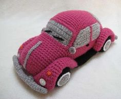 a pink crocheted toy car sitting on top of a white sheet with grey trim