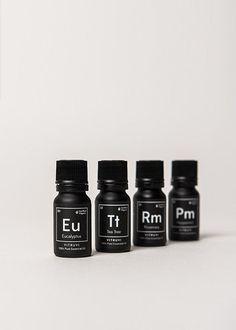 five bottles of essential oils are lined up in a row on a white surface, one is empty and the other has black caps