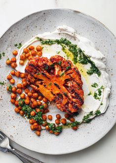 a white plate topped with meat covered in sauce and garnished with chickpeas