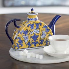 a yellow and blue teapot sitting on top of a table next to a cup of coffee