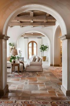 an archway leads into a living room with white furniture and rugs on the floor