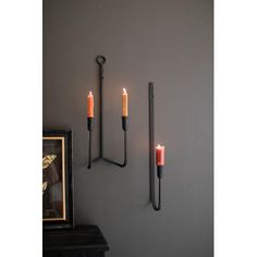 three candles are lit on the wall next to a framed photograph and two iron sconces