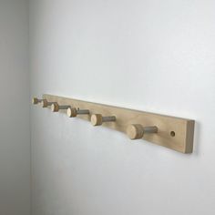 a wooden coat rack with five pegs on it in a white walled room next to a wall