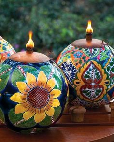 three colorfully painted vases with lit candles in them sitting on a wooden table