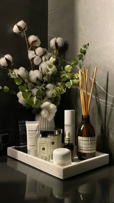 a white tray with some bottles and candles on it next to a vase filled with flowers