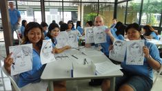 four people sitting at a table holding up paper drawings with faces drawn on them in front of them