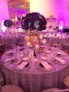 the table is set with silverware and purple flowers in tall vases on each side