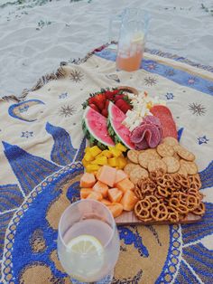 a platter of fruit, crackers and pretzels on a beach towel