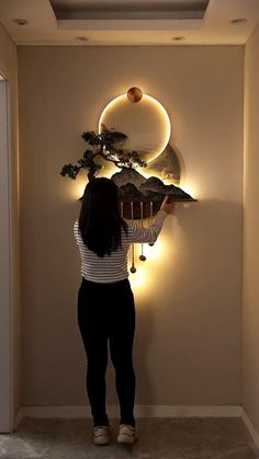 a woman is standing in front of a wall with lights and a bonsai tree on it