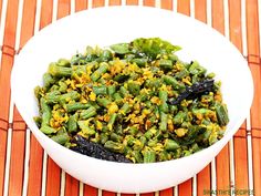 a white bowl filled with green beans on top of a bamboo mat