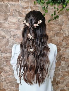 a woman with long hair and flowers in her hair is standing against a stone wall