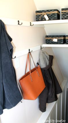 an orange purse hanging on a white shelf next to some black and gray baskets,