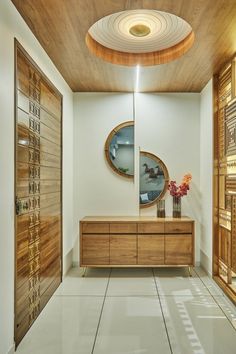 a large wooden cabinet sitting in the middle of a room next to a mirror and vase with flowers on it