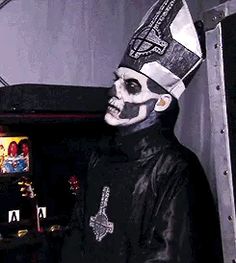 a man in a skeleton mask and top hat standing next to a piano with other musical instruments behind him