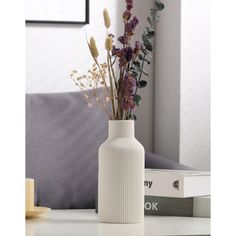 a white vase filled with purple flowers on top of a table next to a gray couch