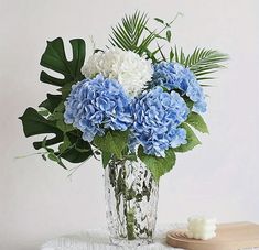 a vase filled with blue and white flowers next to a candle on a doily