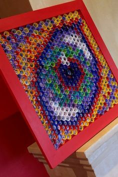 a colorful artwork made out of plastic bottle caps on a red table with a white wall in the background