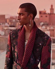 a man wearing a red scarf and earrings standing in front of a cityscape