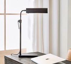 a desk lamp sitting on top of a wooden table next to a window with white curtains