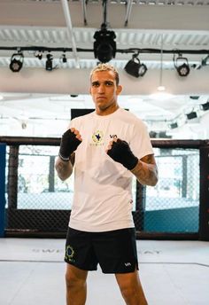 a man standing in a boxing ring with his fists up and wearing black shorts, white t - shirt and gloves